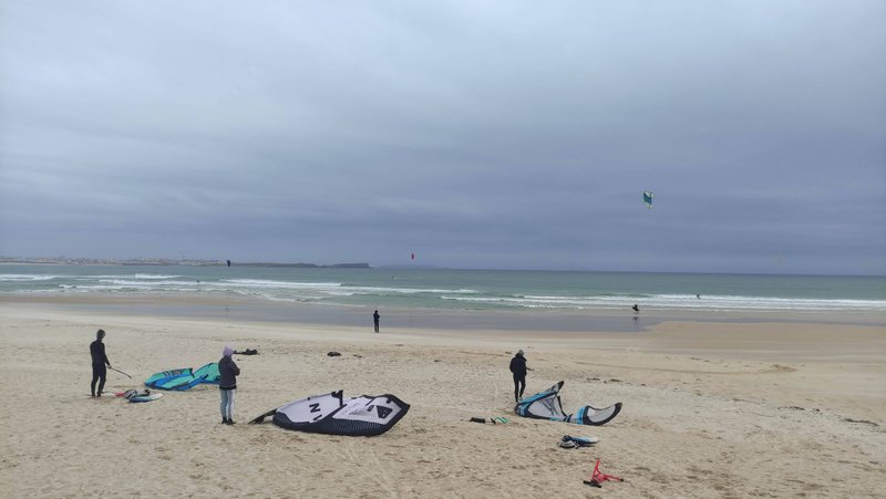 Kitesurfers preparing their equipment on the sandy beach at Cantinho under an overcast sky. — Cantinho (Costa de Peniche), Peniche, Portugal