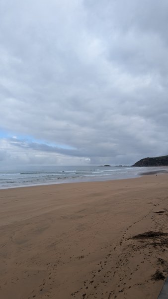 A wide, empty sandy beach with waves under an overcast sky. — Zarautz, Spain