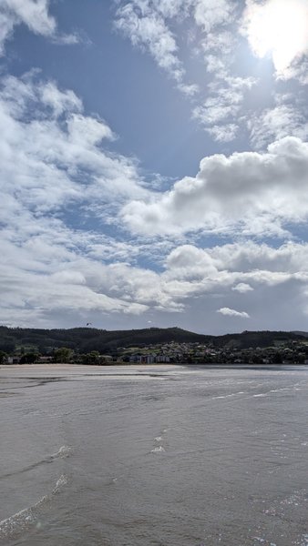 A wide shot of a bay with calm water in the foreground, a town along the distant shore, and hills under a cloudy sky. — Cedeira (Valdoviño), Cedeira, Galicia, Spain