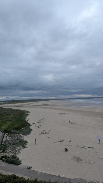 A wide view of Enniscrone beach and dunes under an overcast sky, with the ocean visible in the distance. — Inishcrone / Enniscrone (Enniscrone), Ireland