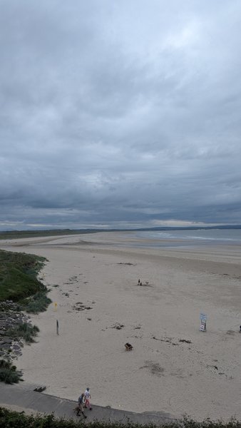 An expansive sandy beach stretches under an overcast sky with distant water. — Inishcrone / Enniscrone (Enniscrone), Ireland