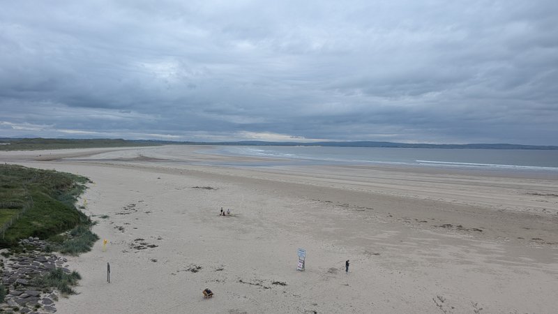 An expansive sandy beach stretches under a cloudy sky with distant hills and calm waters. — Inishcrone / Enniscrone (Enniscrone), Ireland