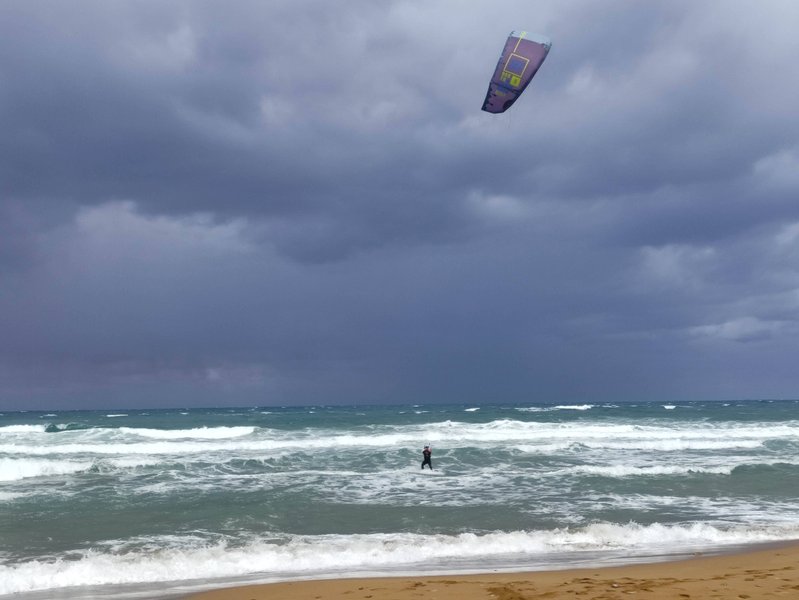 A kitesurfer riding in wavy conditions under a cloudy sky at Stalos beach.