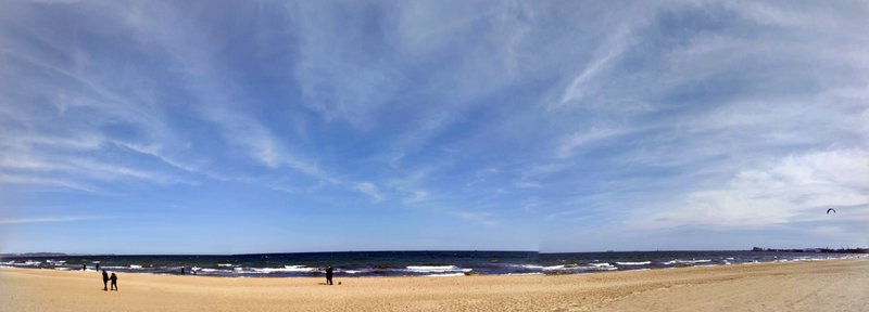 Wide panoramic view of the beach and water in Gdańsk with a kite visible in the sky.