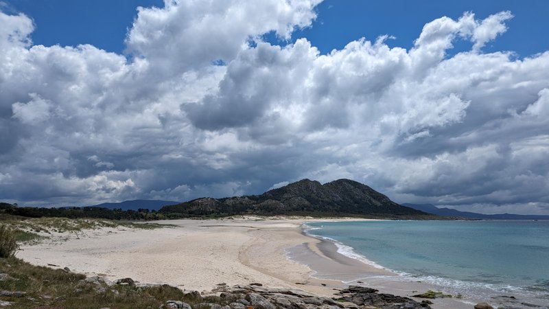A wide view of Ancoradoiro beach with mountains in the background under a cloudy sky. — Ancoradoiro (Louro), Muros, Galicia, Spain
