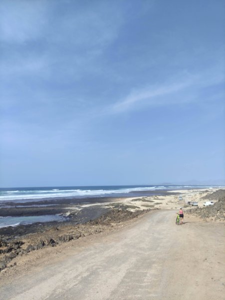A dirt road leads towards the rocky coastline and surf at Derecha de los Alemanes.