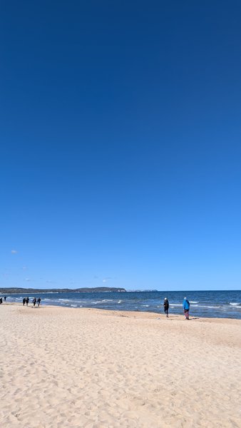A wide sandy beach meets the calm sea under a clear blue sky, with people walking along the shore. — Sopot, Poland
