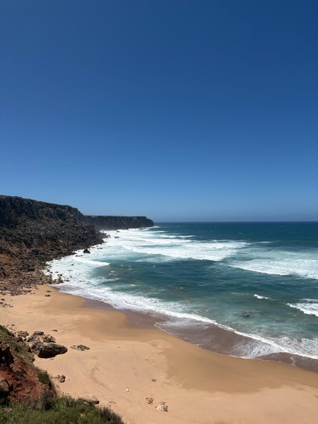 A high-angle view of Telheiro Beach showing the sandy shore, breaking waves, and rugged cliffs. — Praia do Telheiro (Sagres), Sagres, Portugal