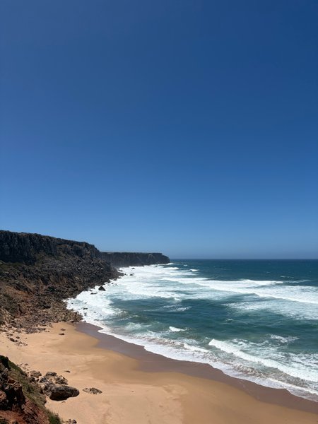 A wide view of Telheiro Beach showing the sandy shore, rocky cliffs, and crashing waves. — Praia do Telheiro (Sagres), Sagres, Portugal