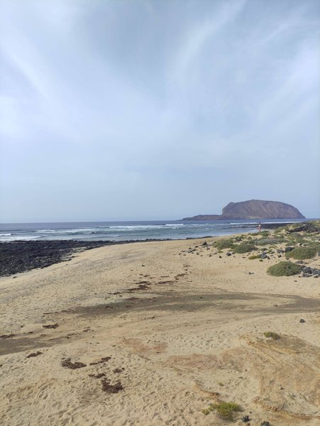 A wide shot of the sandy beach and coastline looking out towards a distant island. — Golden Eye (La Graciosa), Spain