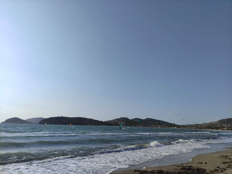 Windsurfers riding on the choppy waters of Anavissos bay under a clear sky.