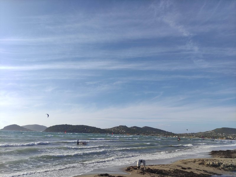 A view of the bay at Anavissos with several windsurfers and a kite on the water.
