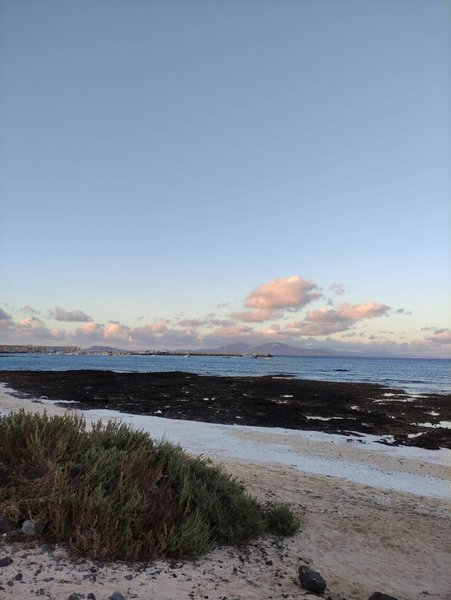 A view of the sandy beach and rocky shoreline at El Muelle under a clear sky.