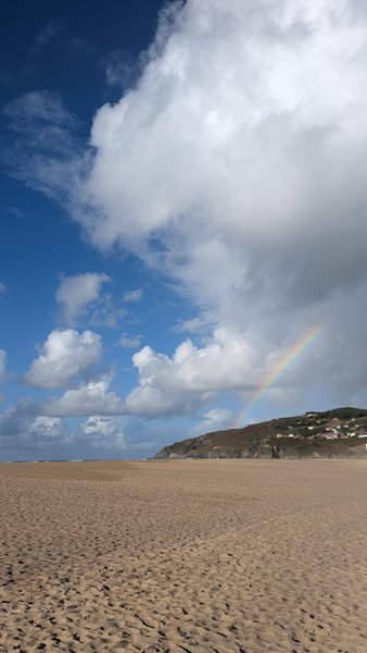 A wide, sandy beach with a distant hill and water, under a partly cloudy sky with a faint rainbow. — Valdoviño (Da Frouxeira), Valdoviño, Galicia, Spain