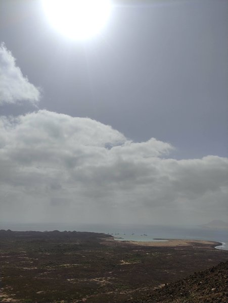 A distant high-angle view of the coastline and ocean under a bright, overexposed sky. — Castillo del Rubicón (Playa Blanca), Spain
