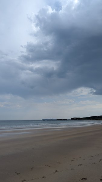 A wide view of the sandy beach and coastline at White Park Bay under a cloudy sky.
