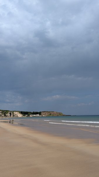 A wide view of the sandy beach and bay at White Park Bay under a cloudy sky.