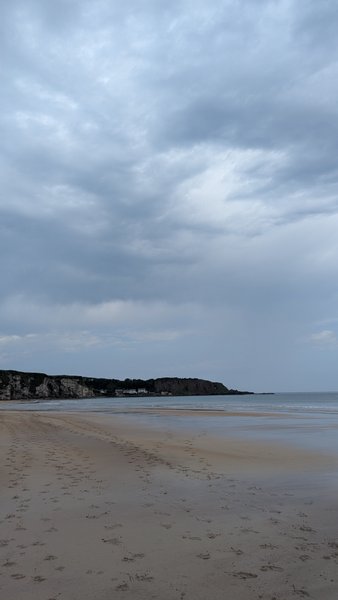 A wide sandy beach at White Park Bay with cliffs in the distance under a cloudy sky.