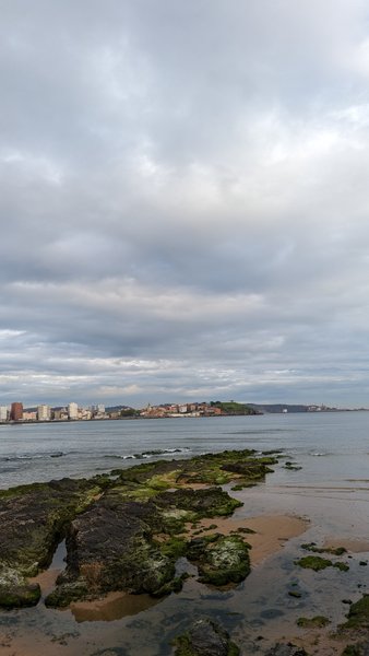 A view of the rocky shoreline and coastal waters at La Roca, Gijón, with the city skyline in the distance. — La Roca (Gijón), Gijón, Asturias, Spain
