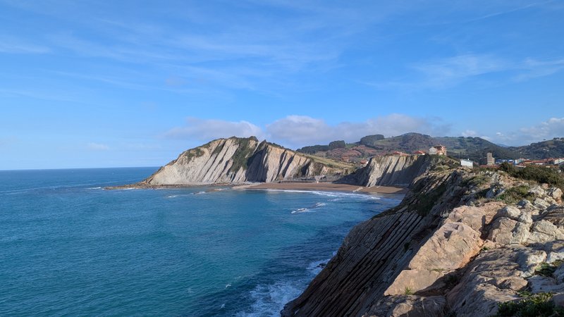 A panoramic view of the layered cliffs, beach, and ocean at Zumaya under a clear blue sky.