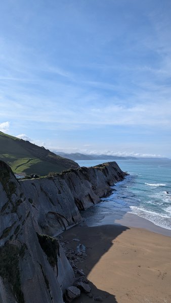 An aerial view of a rugged coastline with a sandy beach and cliffs meeting the ocean under a clear sky. — Zumaya, Spain