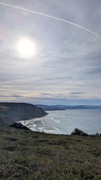 An elevated view of the Barrika coastline with waves breaking on the shore under a partly cloudy sky. — Barrika (Pais Vasco), Sopela, Autonomous Community of the Basque Country, Spain