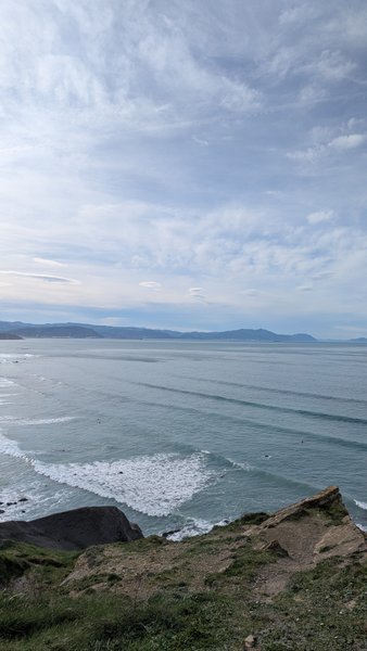 An aerial view shows the coastline of Barrika with waves breaking and small figures in the water. — Barrika (Pais Vasco), Sopela, Autonomous Community of the Basque Country, Spain
