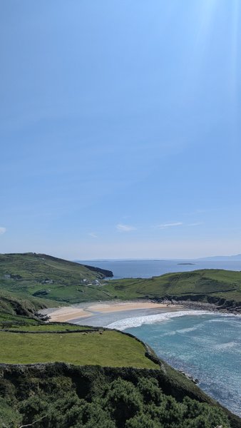 An aerial view of a sandy bay with turquoise water surrounded by green hills under a clear blue sky. — Muckros (Península de Muckross), Ireland