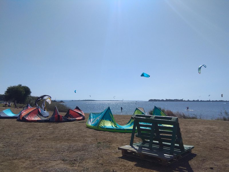 Kitesurfing equipment on the grassy launch area at Lo Stagnone with kites visible in the air over the water. — Lo Stagnone (Marsala), Marsala, Sicily, Italy