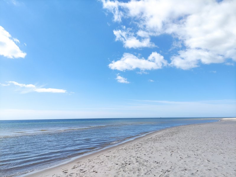 A wide sandy beach meets the blue water under a partly cloudy sky. — Sandhammaren, Sweden