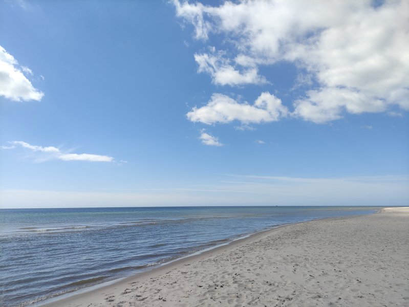 A wide sandy beach meets the calm sea under a bright blue sky at Sandhammaren.
