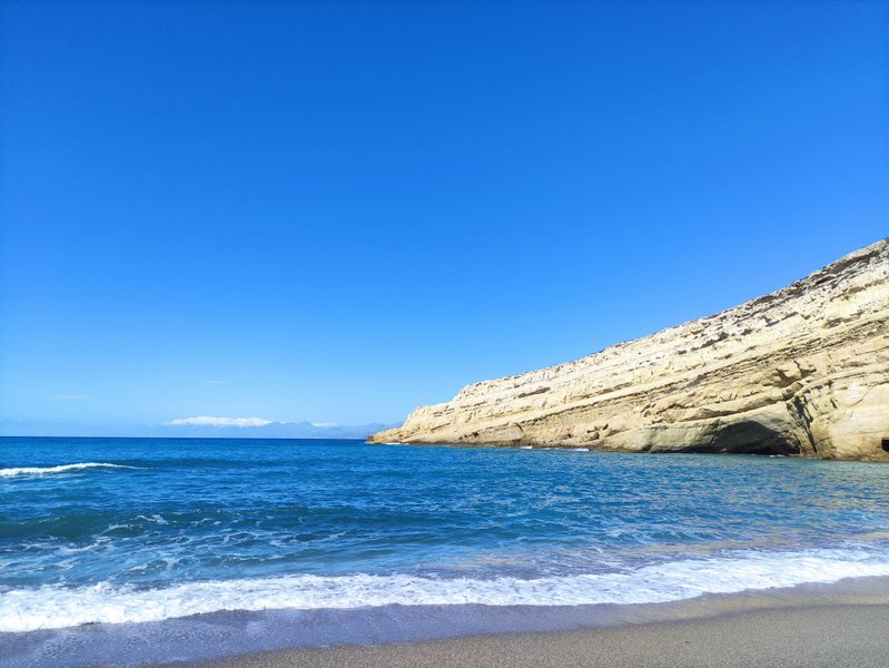 A wide view of Matala beach and its iconic limestone cliffs under a clear blue sky. — Matala (Crete), Tybakio Municipal Unit, Greece