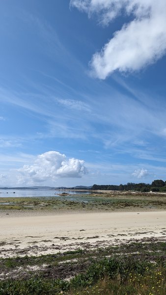A wide view of the sandy beach and calm waters at A Illa de Arousa under a bright blue sky.