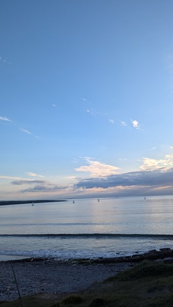 A view of the bay at Rosses Point with small sailboats on calm water at dusk.