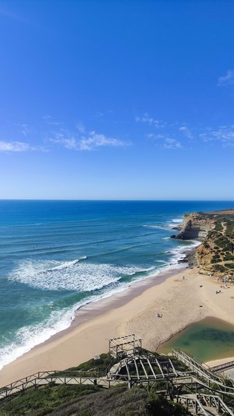 A wide, elevated view of Ribeira das Ilhas beach showing the wave lines and coastline.