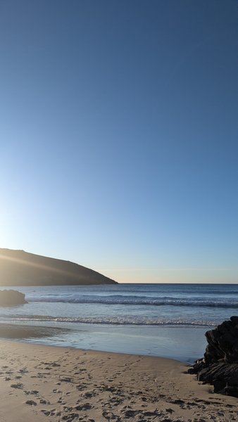A view of the sandy beach and breaking waves at El Baleo under a clear blue sky.