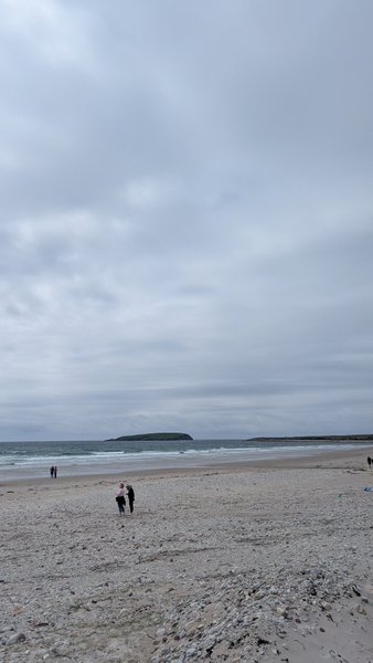 A wide view of Keel Beach with people walking on the sand and an island in the distance under a cloudy sky. — Keel (Ilha de Achill), County Mayo, Westport-Belmullet Municipal District, Ireland