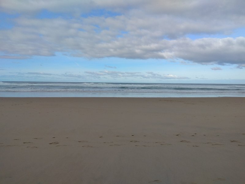 A wide view of the sandy beach and ocean under a cloudy sky. — Cresmina (Cascais), Cascais, Portugal