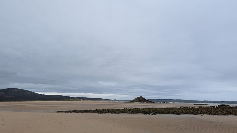 A wide view of the sandy beach and rocky outcrops at Playa de Ladeira under an overcast sky. — Playa de Ladeira (A Barbanza), Santa Uxía de Ribeira, Galicia, Spain