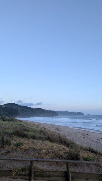 A wide view of Tairua Beach showing the surf and coastline under a clear sky. — Playa de Tairua, Tairua, Waikato, New Zealand