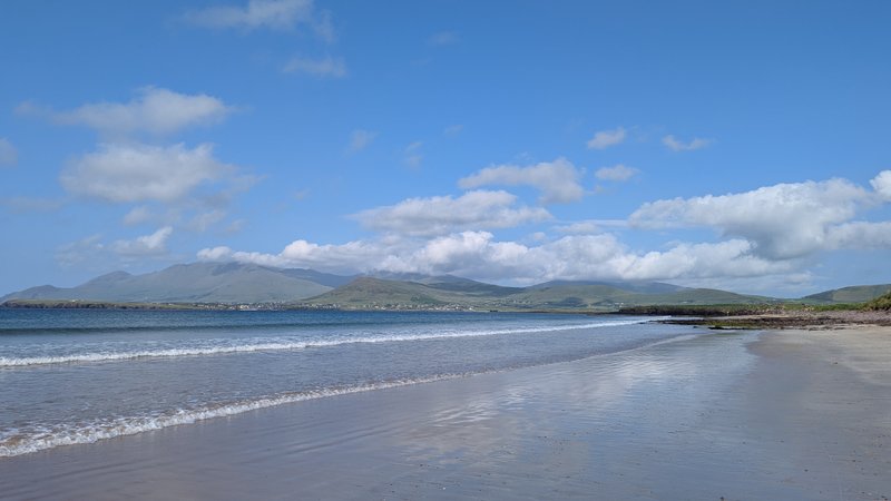 A wide view of the sandy beach and clear blue water at Smerwick Harbour.