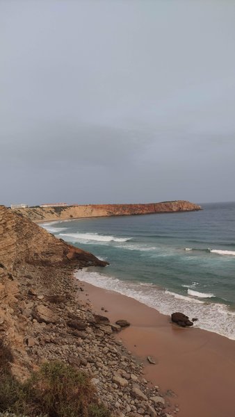A high-angle view of Mareta beach and the surrounding cliffs under an overcast sky.