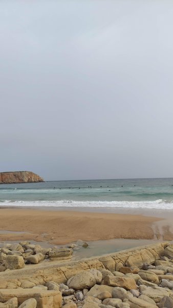 View of Mareta beach with surfers in the water and a rocky cliff in the distance.