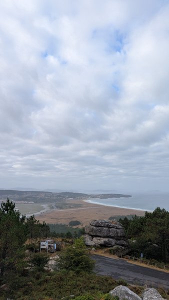 An elevated panoramic view of a long sandy beach and estuary, with forested hills and a cloudy sky. — Mexilloeira (Balea), O Grove, Galicia, Spain