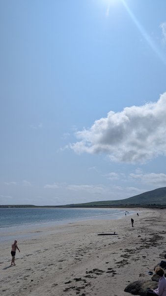 A wide view of Ventry Beach showing the sandy shoreline and bay under a bright sky.