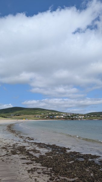 A view along the sandy shoreline of Ventry beach looking across the bay toward the green hills.