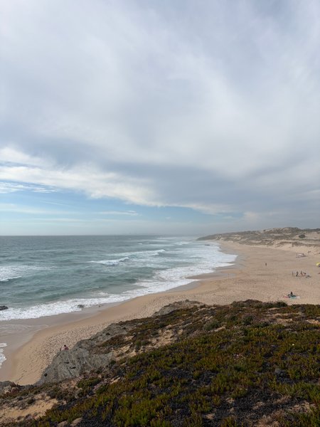 A wide-angle view of the beach and surf at Malhão from an elevated position.