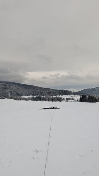 A vast snowy field extends towards a line of forested mountains under an overcast sky. — Oravske Vesele, Oravské Veselé, Slovakia