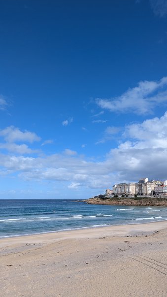 A view across Playa de Orzán showing the sandy beach and the water's edge with buildings in the distance. — Praia de Orzán, A Coruña, Galicia, Spain