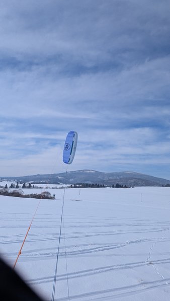 A foil kite flies over a snow-covered field in Kapliczka Orava.